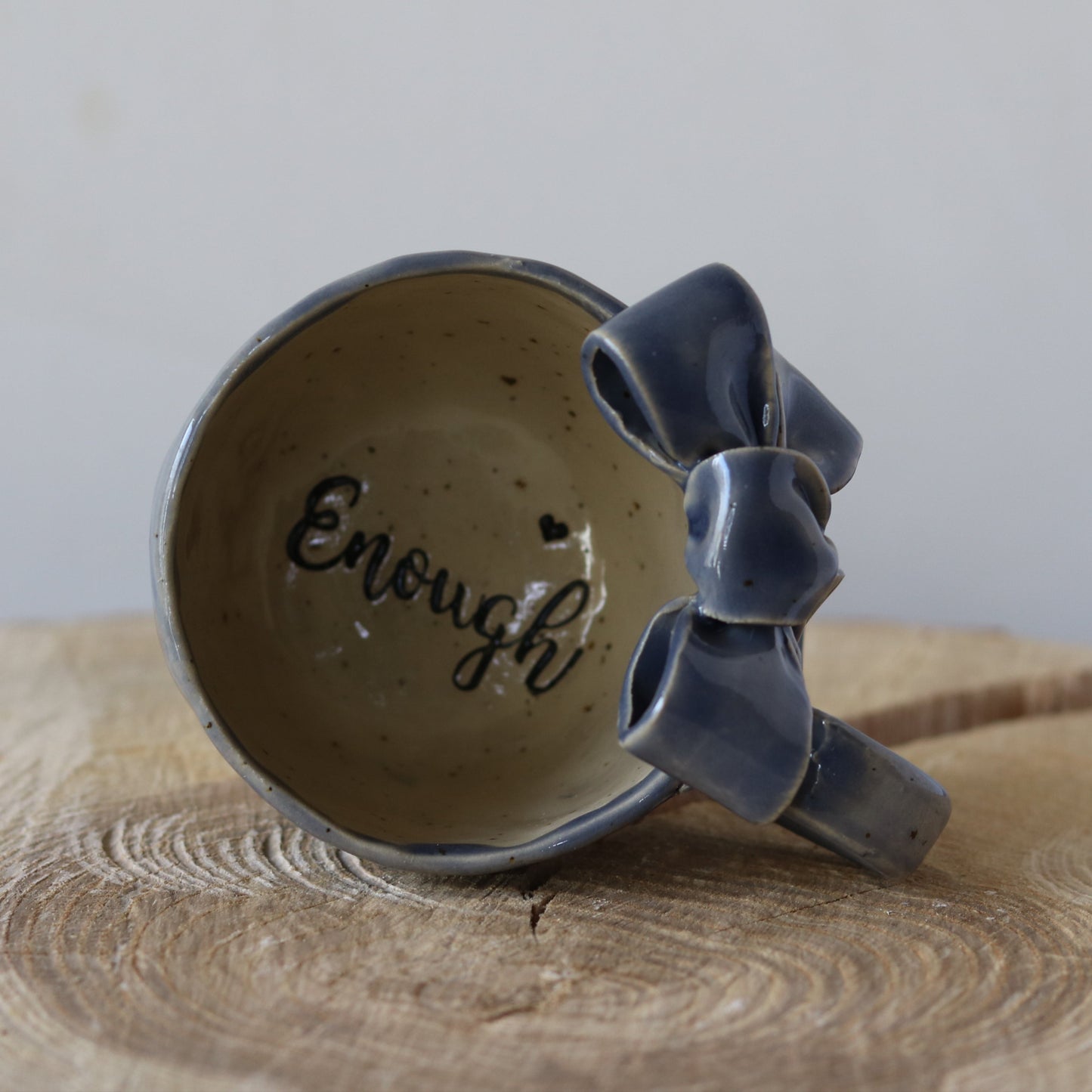Blå kaffekop med hank. sløjfe på kanten og teksten Enough i bunden